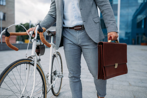 Uomo d'affari in giacca e cravatta con valigetta e bicicletta in centro. Persona d'affari a cavallo del trasporto ecologico sulla strada della città
 - Foto, immagini