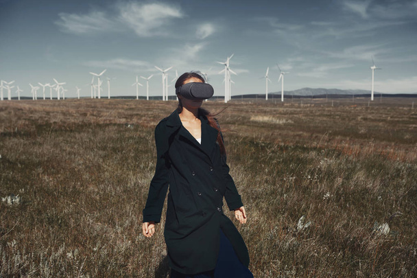 Жінка в гарнітурі VR на полі поруч з вітровими турбінами
 - Фото, зображення