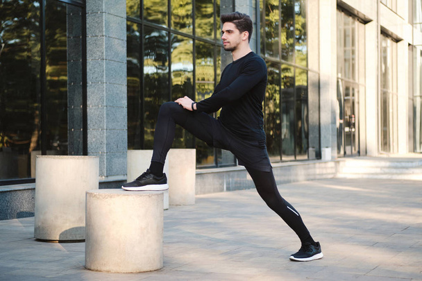Vista lateral de jovem atraente confiante desportivo homem fazendo exercícios durante o treino na rua
 - Foto, Imagem