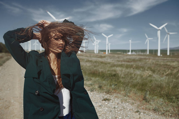 Mulher com longos cabelos desarrumados ao lado da turbina eólica com o w
 - Foto, Imagem