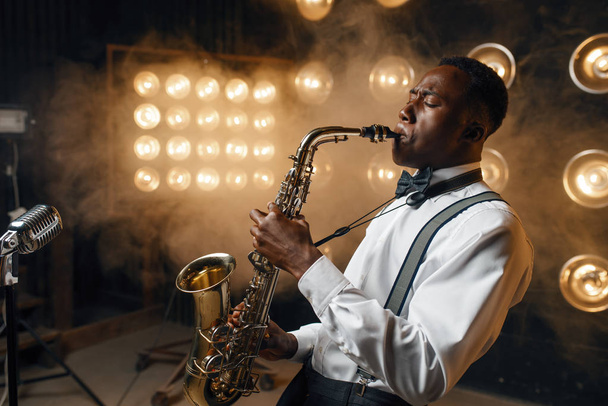Африканский джазовый исполнитель играет на саксофоне на сцене с прожекторами
 - Фото, изображение