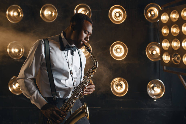 Hombre jazzman toca el saxofón en el escenario con focos
 - Foto, Imagen