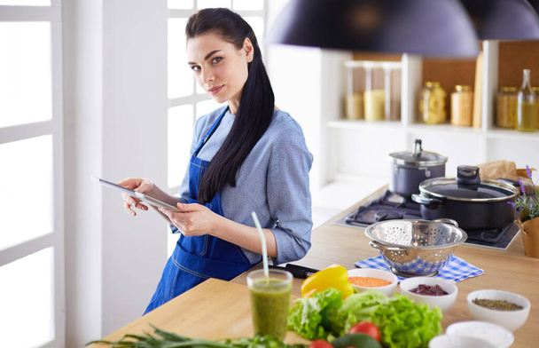 Young woman using a tablet computer to cook in her kitchen - Foto, Bild