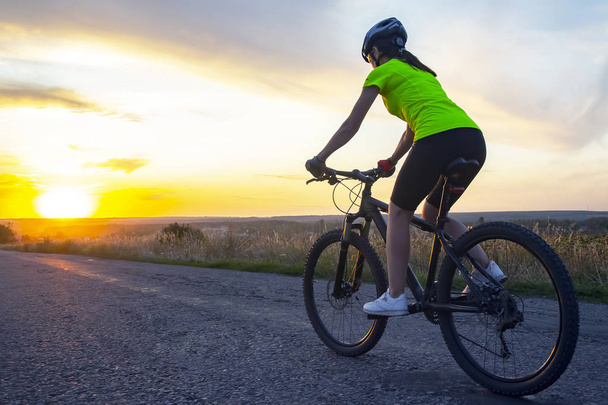 Kaunis tyttö pyöräilijä ratsastaa polkupyörällä tiellä auringonlaskussa
 - Valokuva, kuva