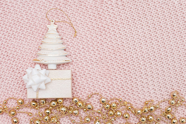 Decorative beige christmas tree, gift box and gold garland on pink knitted background. New Year or Christmas concept. Top view Flat lay Template for design, greeting card, invitation - Photo, image