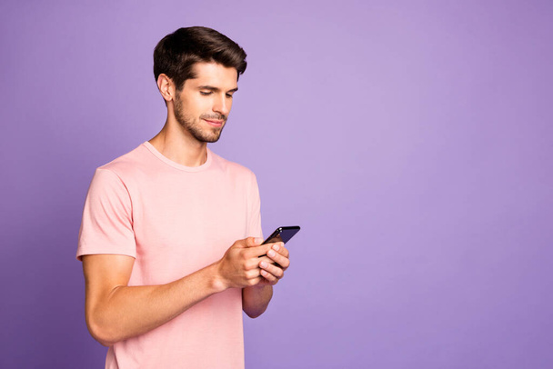 Profile side view portrait of his he nice attractive calm focused guy wearing pink tshirt holding in hands using 5g cell wi-fi connection isolated over violet purple lilac pastel color background - Valokuva, kuva