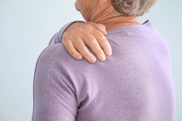 Mulher idosa que sofre de dor no ombro contra fundo claro, close-up
 - Foto, Imagem