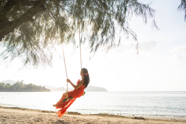 girl in a red dress on a swing among tropical palm trees in Thailand at sunset - Photo, image