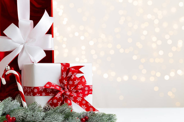 Cajas de regalo blancas y rojas de Navidad con cinta roja por algunas ramas de abeto o pino nevado con conos y bayas rojas sobre un fondo claro brillante con bokeh natural y espacio de copia
. - Foto, imagen