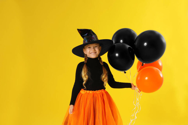 Cute little girl with balloons wearing Halloween costume on yellow background - Фото, зображення