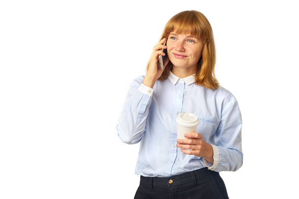 Portrait of pensive redheaded woman with freckles holding coffee to go cup in hand and talking on smartphone isolated on white background   - Foto, Imagem