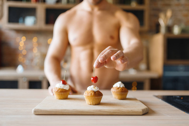 Çıplak vücutlu bir adam mutfakta kirazlı kek pişiriyor. Çıplak bir erkek evde kahvaltı hazırlıyor, kıyafetsiz yemek hazırlıyor. - Fotoğraf, Görsel
