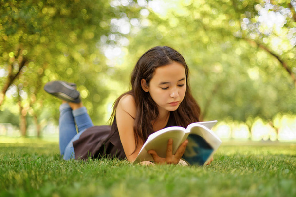 Kazakh beautiful girl reading a book in the summer park - 写真・画像