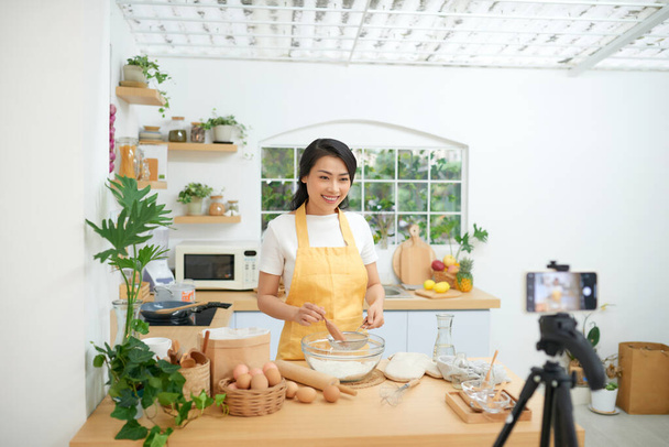 Bastante joven asiática bloguera de comida trabajando en un nuevo video y explicando cómo cocinar un plato
 - Foto, Imagen