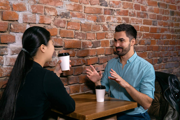 junger Mann spricht über etwas mit einem Mädchen, das an einem Tisch in  - Foto, Bild