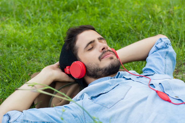 Молодой человек расслабляется и слушает музыку на траве
. - Фото, изображение