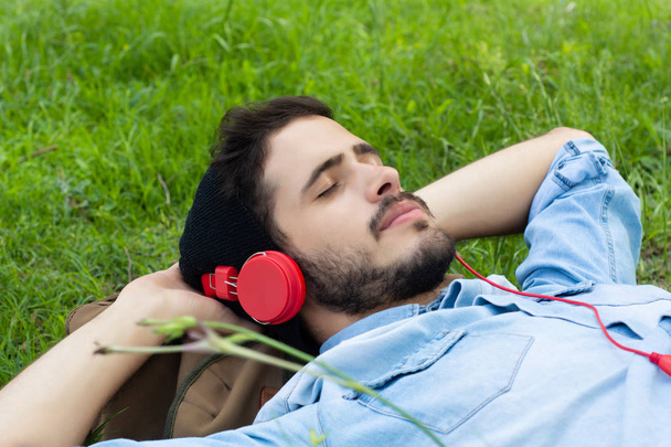 Jeune homme relaxant et à l'écoute de la musique sur l'herbe
. - Photo, image