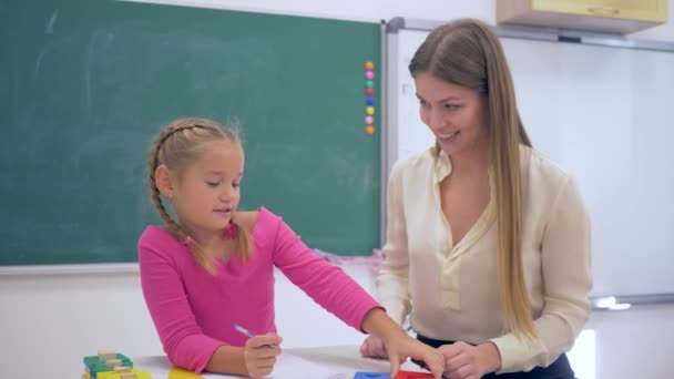 Bireysel eğitim, deneyimli bir öğretmen okul sınıfında tahtaya yakın masada akıllı bir kıza öğretmenlik yapıyor. - Video, Çekim
