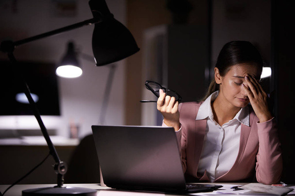 Молодая деловая женщина касается головы, сидя на рабочем месте с ноутбуком устал от работы в офисе - Фото, изображение