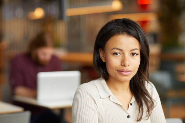 Retrato de una joven hermosa mujer con cabello largo oscuro mirando a la cámara mientras está sentada en la cafetería - Foto, Imagen
