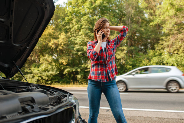 Young woman calling a tow truck on road, car breakdown. Broken automobile or emergency accident with vehicle, trouble with engine on highway - Photo, Image