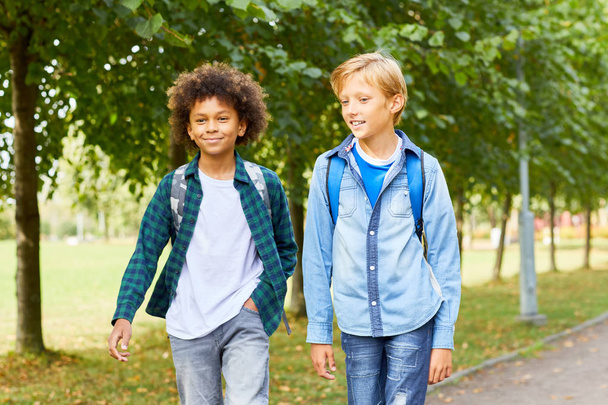 Багатоетнічні хлопчики з рюкзаками йдуть разом по дорозі, повертаючись зі школи
 - Фото, зображення