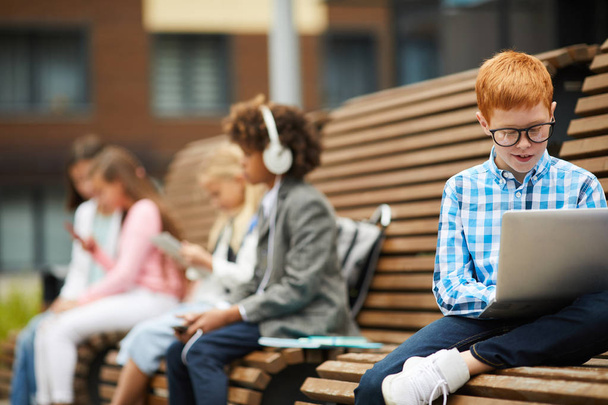 Группа детей, сидящих на скамейке после школы, отдыхающих на открытом воздухе
 - Фото, изображение