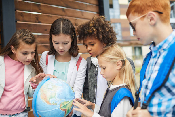 Grupo de crianças de escolas multiétnicas apontando para o globo aprendendo a geografia
 - Foto, Imagem