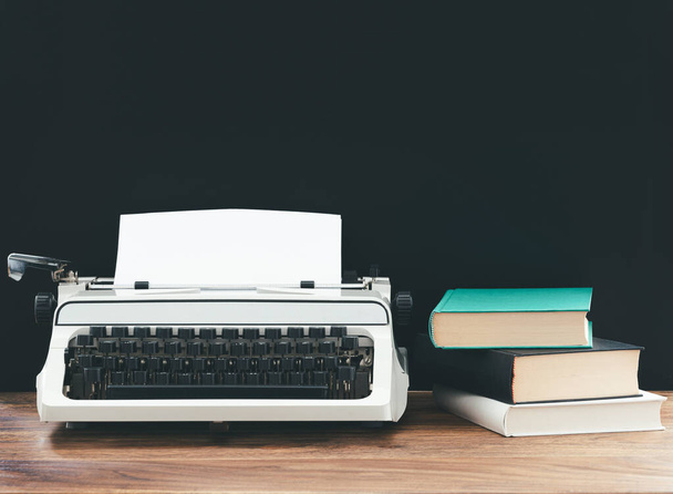 máquina de escrever vintage e pilha de livros em mesa de madeira rústica contra fundo preto
 - Foto, Imagem