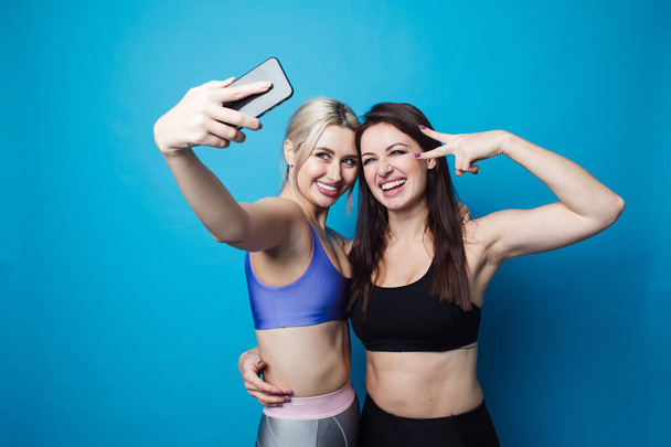 Two happy and cheerful girls dressed in fitness bodysuits, best friends have fun and take selfies - Valokuva, kuva