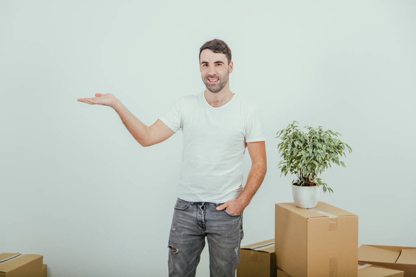 Handsome young man moving into new house, standing with hand in pocket, pointing into copy space for text or product on the side. - Fotoğraf, Görsel