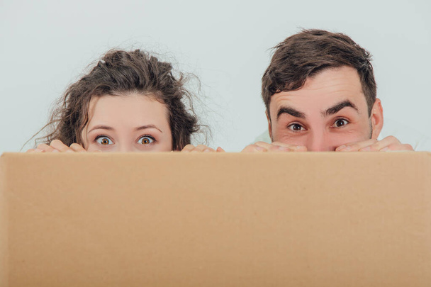 Grappige vrouw en echtgenoot verbergen zich achter de grote kartonnen doos, samen, dwaas kijkend naar de camera. - Foto, afbeelding