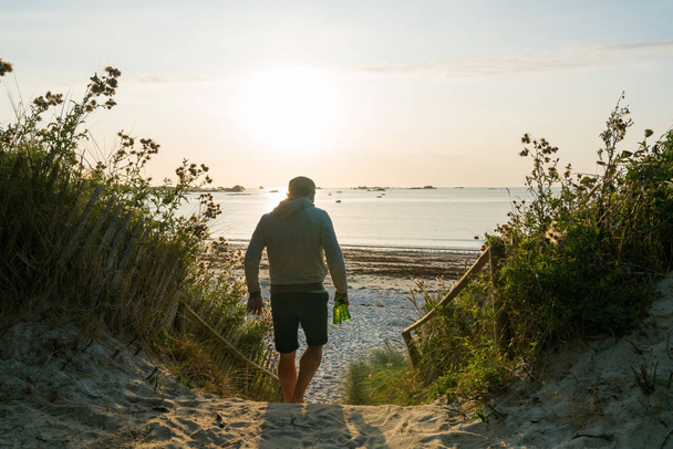 розслаблений молодий чоловік іде на милий пляж на заході сонця з пивними пляшками в руці. - Фото, зображення