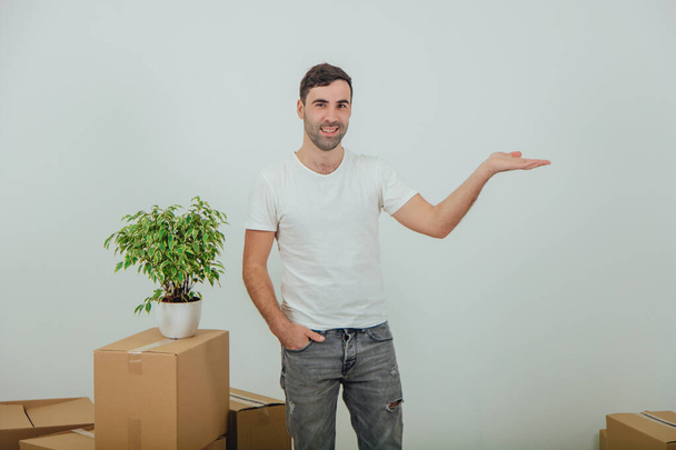Handsome young man moving into new house, standing with hand in pocket, pointing into copy space for text or product on the side. - Foto, Imagem