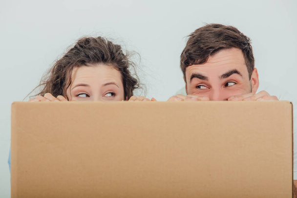 Divertida esposa y marido escondidos detrás de la caja de cartón grande, juntos, mirándose el uno al otro
. - Foto, Imagen