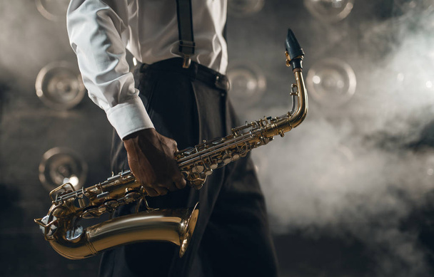Black jazz musician with saxophone on the stage with smoke. Black jazzman holds instrument in hands - Zdjęcie, obraz