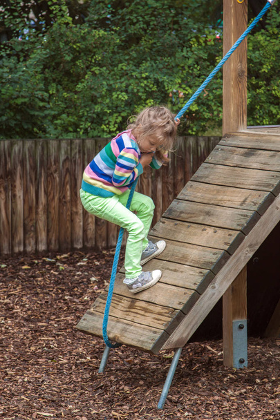 girl climbs a rope on a wooden slope on a modern Playground outdoors - Foto, immagini