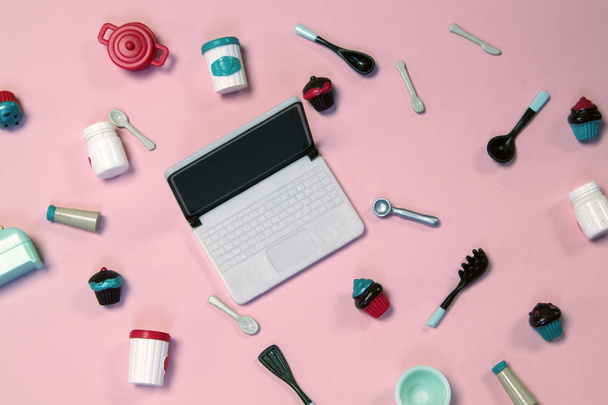 flat lay image of plastic toy tableware with cakes and laptop on pastel pink background - Fotó, kép
