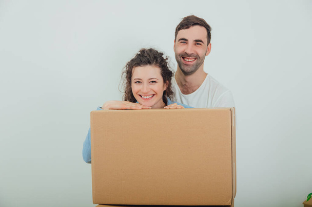 Uśmiechnięta żona i mąż stojący za wielkim pudełkiem kartonowym, razem, przytulający się, patrzący w kamerę. - Zdjęcie, obraz