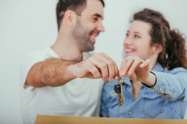 Freudestrahlend stehen Frau und Mann hinter dem großen Karton und halten vor der Kamera die Schlüssel für ihre neue Wohnung zusammen . - Foto, Bild