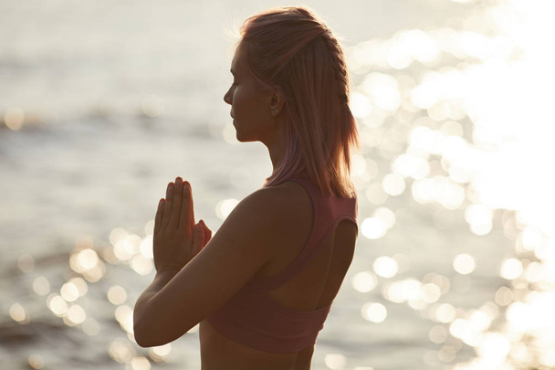Rear view of young woman with blond hair standing with eyes closed and meditating against the sea outdoors - Photo, Image
