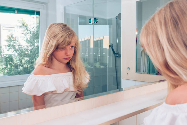 triest blond meisje alleen in de badkamer op zoek naar in spiegel - Foto, afbeelding