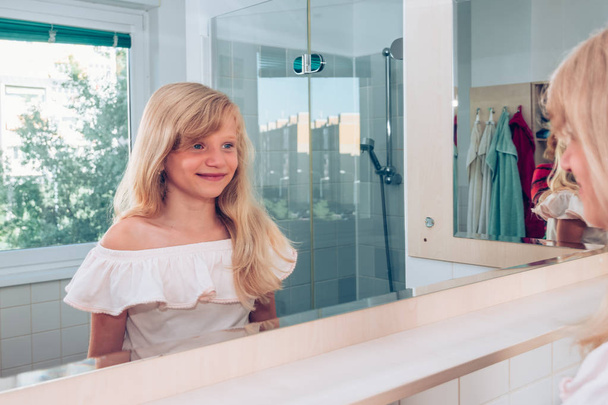 charming blond girl smiling in the bathroom in front of the mirror - Photo, Image