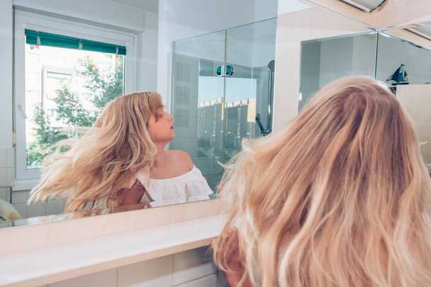 charming blond girl in front of in the mirror - 写真・画像