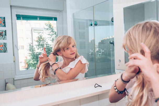 ihana vaalea lapsi kampaa hiuksensa kylpyhuoneessa peilin edessä - Valokuva, kuva