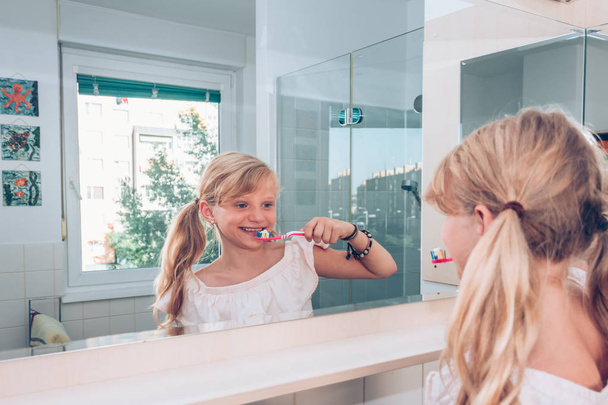 Прекрасная блондинка чистит зубы перед зеркалом в ванной. - Фото, изображение