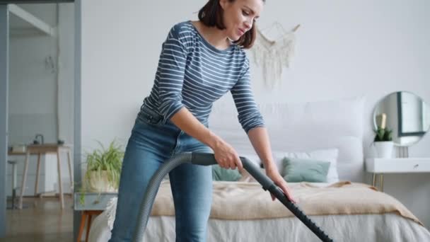 Tilt-down of young lady cleaning carpet with vacuum cleaner in bedroom - Filmmaterial, Video