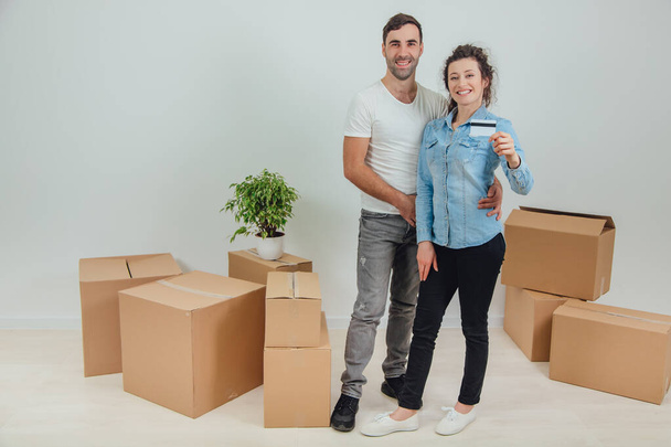 Husband is hugging his wife. Pretty wife is holding a credit card. They are smiling, surrounded by carton boxes. - Photo, Image