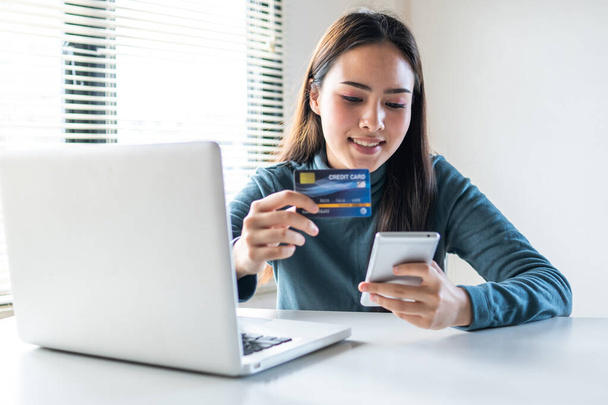 улыбающаяся женщина расплачивается кредитной картой и совершает покупки онлайн по телефону - Фото, изображение