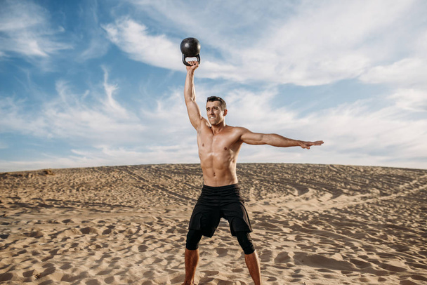 Mužský atlet cvičí s činkami v poušti za slunečného dne. Silná motivace ve sportu, silný venkovní trénink - Fotografie, Obrázek